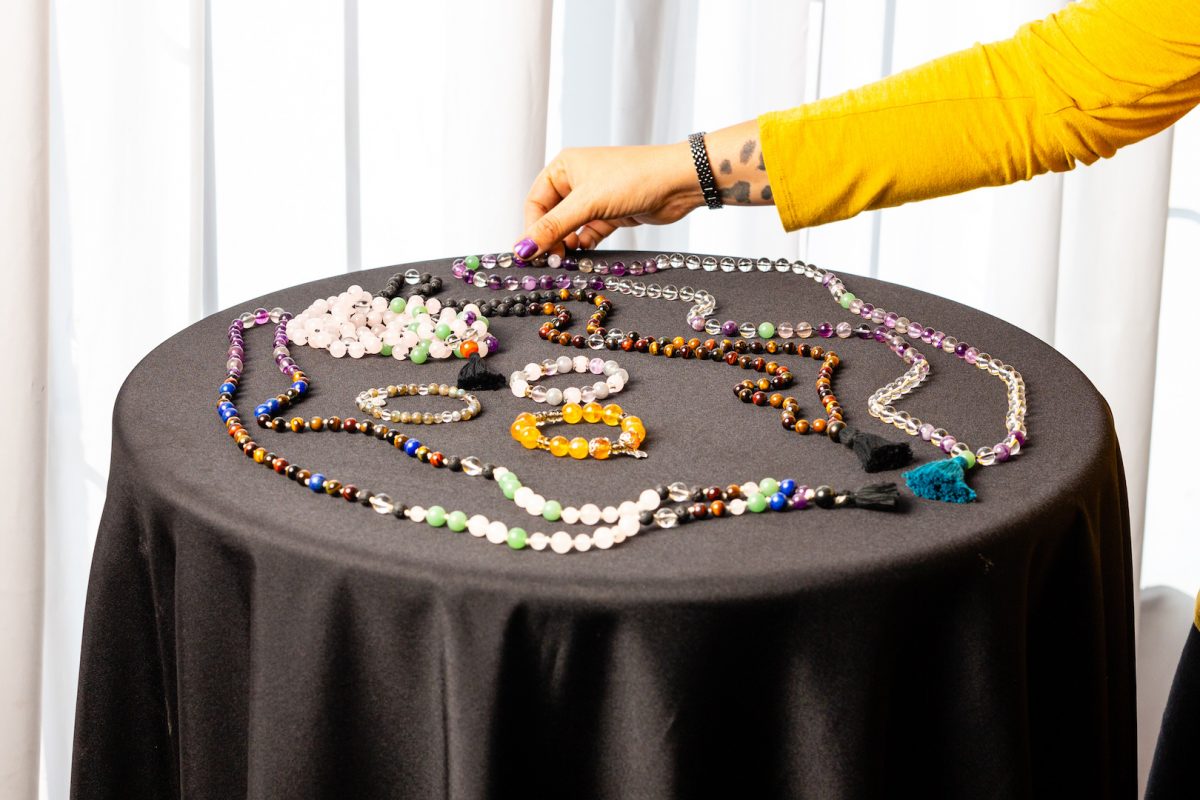 An assortment of mala beads and bracelets. A woman reaches in to select the beads on the right side of table.