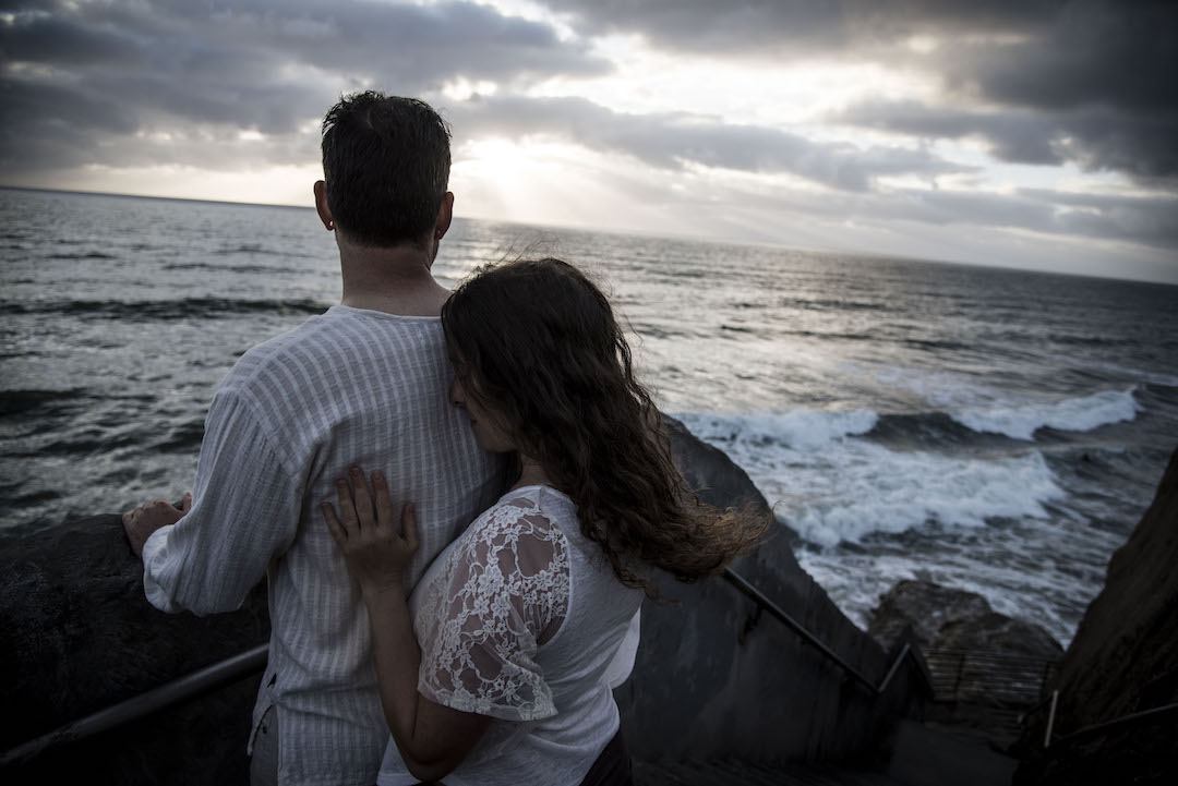 Woman standing behind a man looking at the sea on a beautiful cloudy afternoon