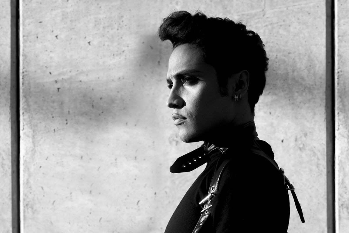 B&W portrait of young man in leather jacket against cement wall profile view.