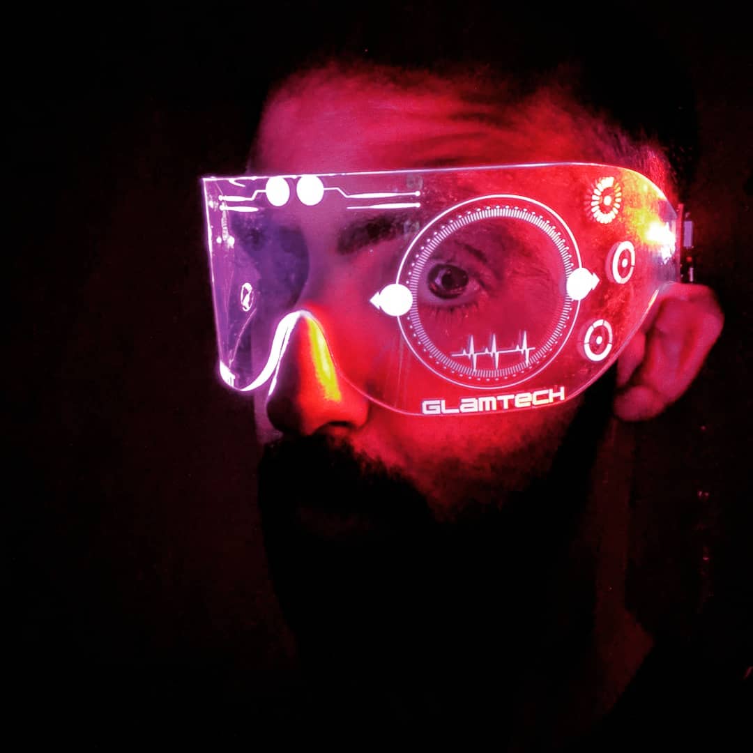 Man in dark room at a party wearing goggles with pink light on him.