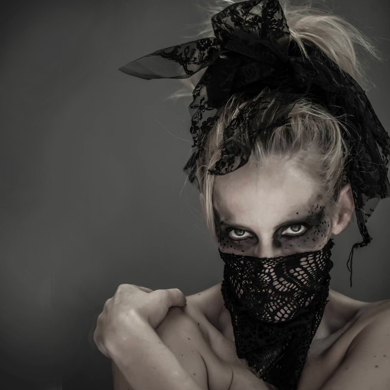 Ballerina looking with intensity at the camera grabbing her right arm with left hand and with her face partially covered by a screened scarf