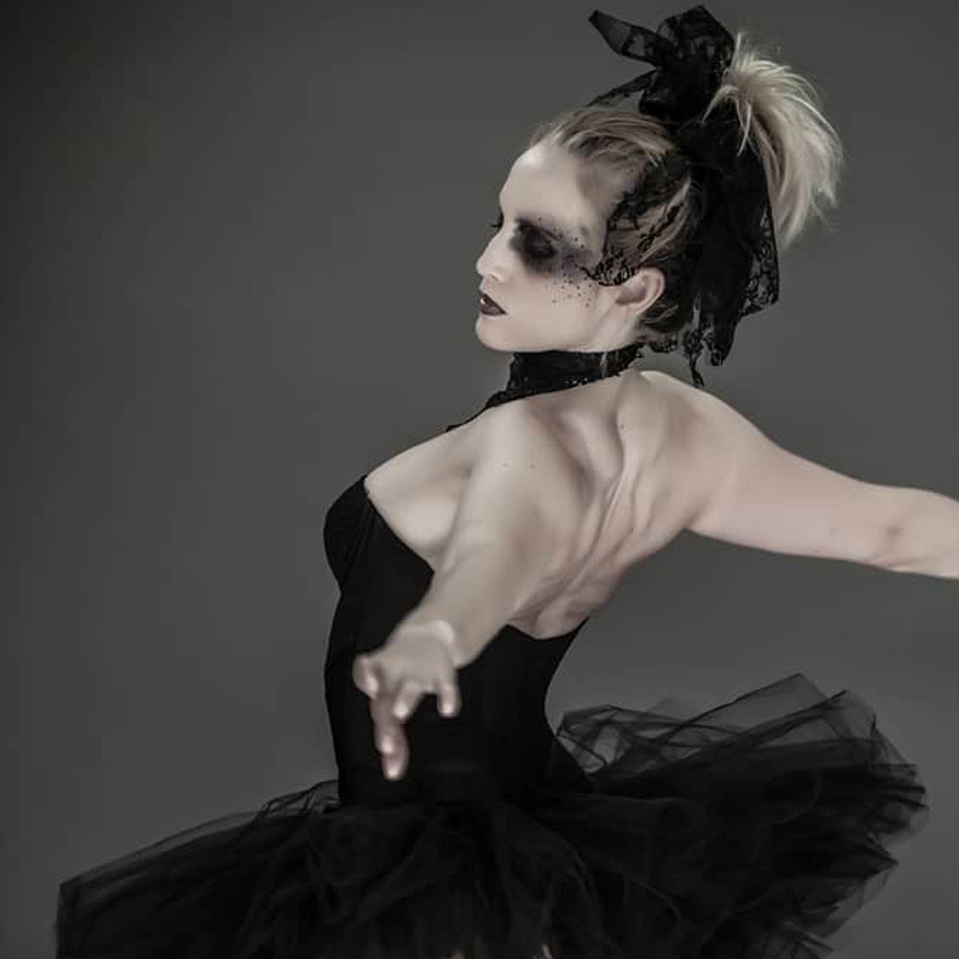 Ballerina with arms spread dancing back to the camera, wearing a black tutu skirt