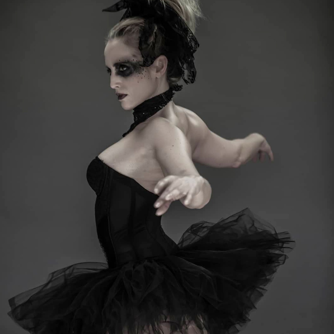 Ballerina with arms spread dancing back to the camera, wearing a black tutu skirt