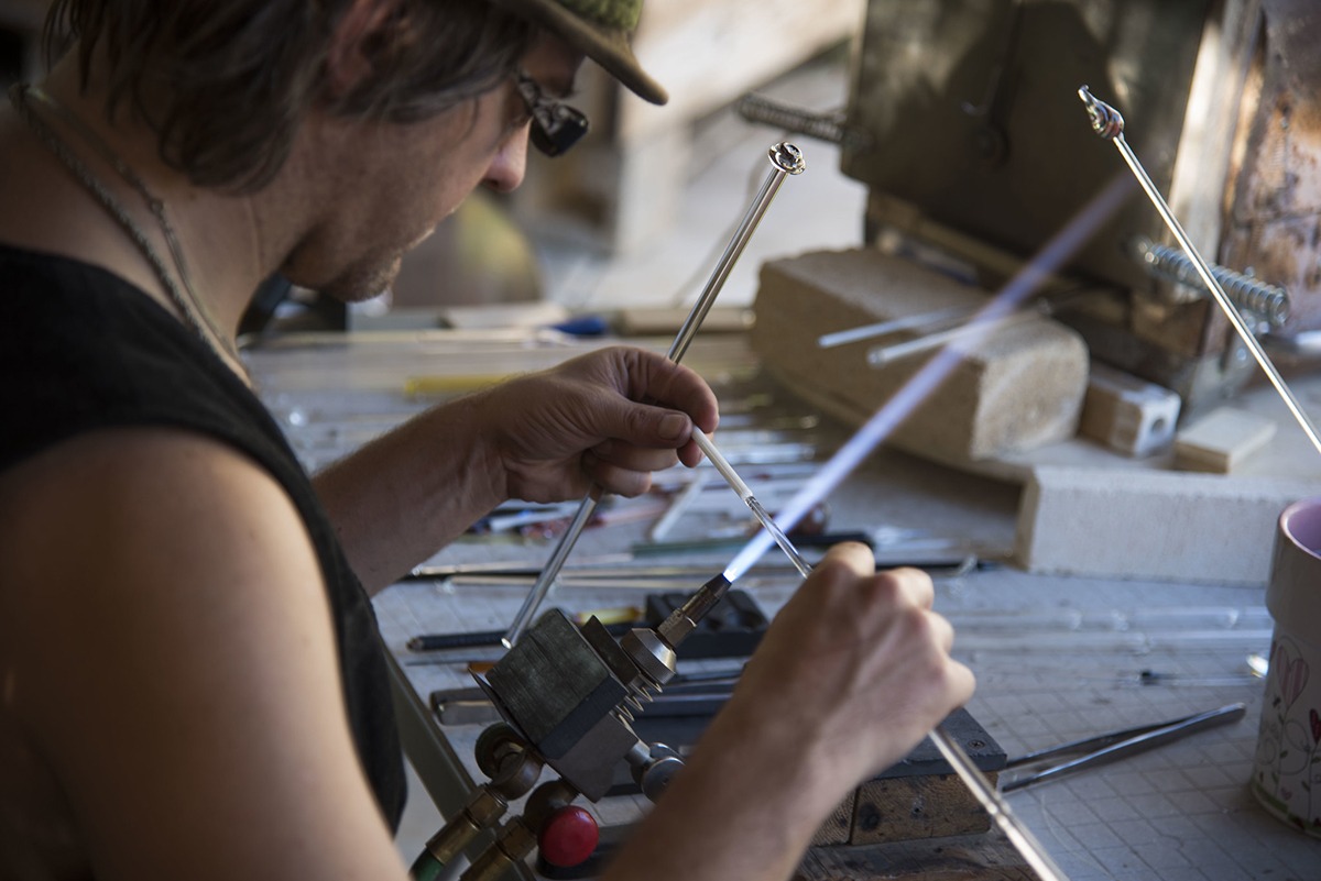 Glass artist Corey Mitchell is holding a thin glass tube against the blow torch flame.