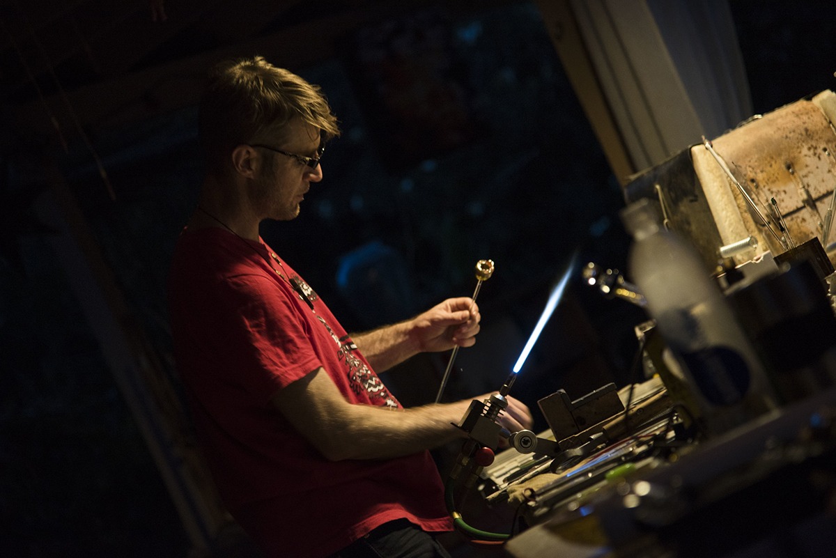 Glass artist, Alexander Chacona regulating the flame of the torch while looking at the nice form he's getting on the piece of glass.