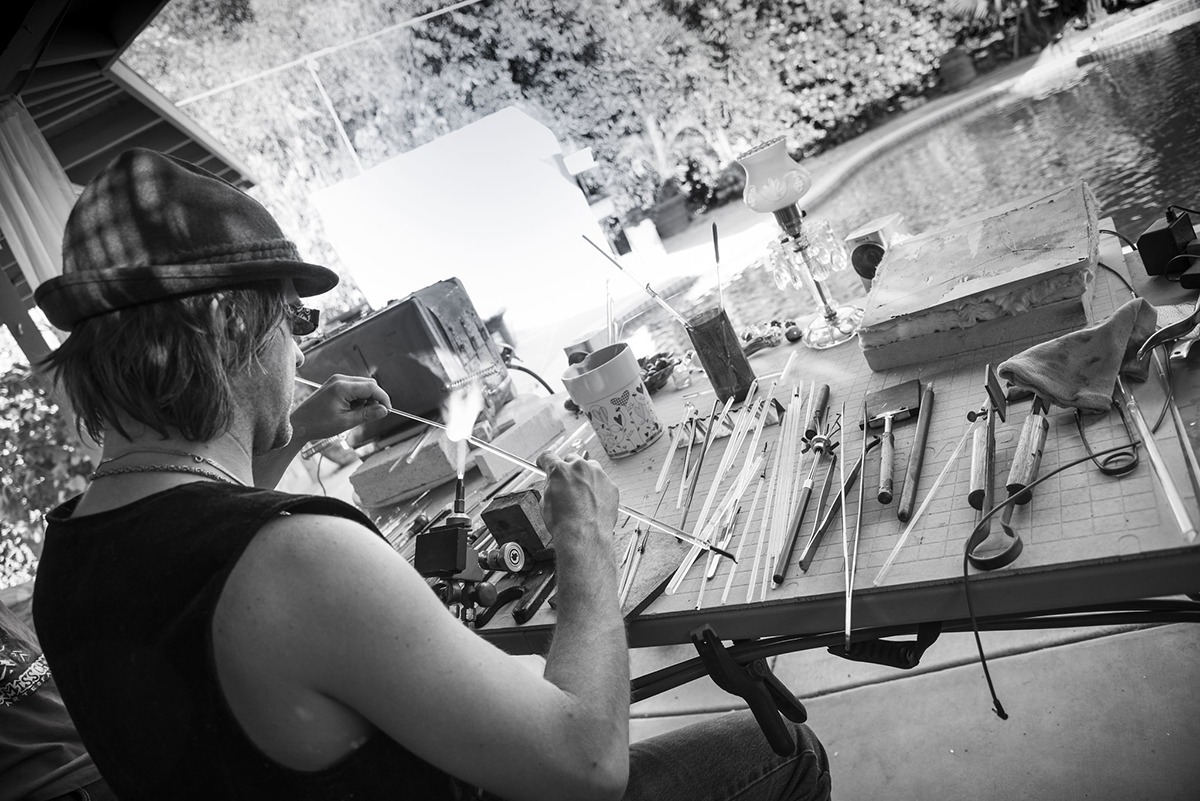 B & W shot of glass artist Corey Mitchell, giving a new form to a tube of glass on a torch flame.