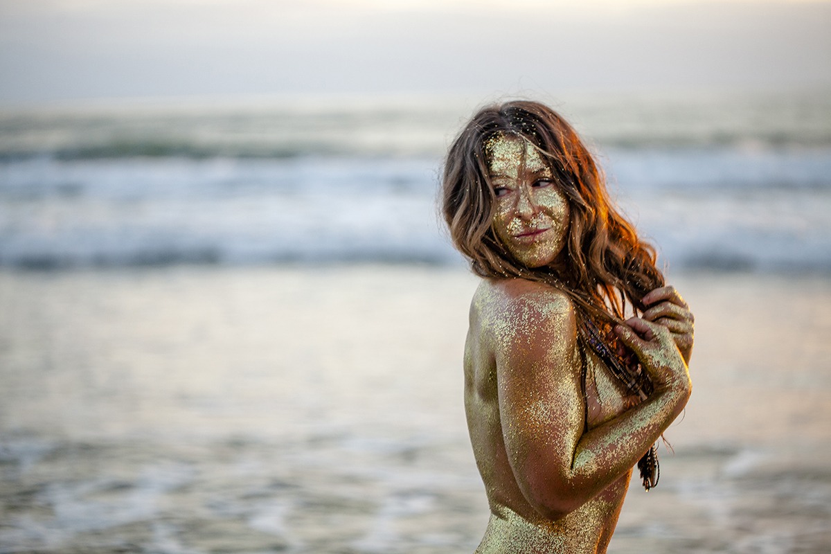 Golden woman at the shoreline, pleasantly looking back over her shoulder towards land. From the Secrets of the Stars series photos by Jon Medel